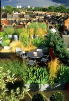 Roof garden with decking, metal furniture and square metal containers planted with grasses