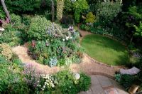 Small shady garden with circular lawn and gravel paths