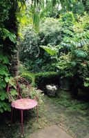 Shady garden with patio area with pink painted chair and view of garden beyond.