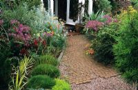 Brick path in front garden at Anne Swithenbank's Garden in Surrey planted with Festuca gauteiri, Yucca 'Golden Sword', Geranium palmatum and Aeonium.