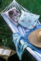 Striped Hammock with cushions, hat and shawl and glass of white wine with open book on small wooden table at Rose Cottage