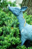 Blue verdigris deer in garden with hebe shrub