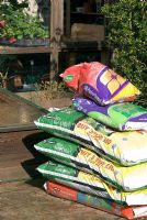 Bags of multi purpose compost, mini bark chippings, lawn dressing and bulb compost  by the green house and cold frame