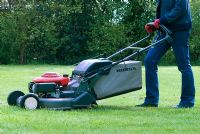 Woman mowing the lawn with a petrol driven rotary mower