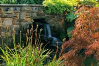 Waterfall and stream underneath footbridge. Iris and acer growing in foreground 