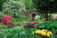 The Dell Garden, Bressingham, Norfolk -  View of flint bridge built by Alan Bloom with mixed borders with perennials, shrubs and bulbs either side 