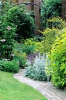 Curved brick path with borders,lawn and clematis growing up arch