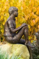 Statue 'Boy on a Rock' by Jane Hogben in front of Cornus sanguinea 'Midwinter Fire' in autumn colour