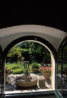View through open window to Mediterranean style garden beyond with containers and ornament on patio - Corfu