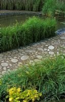 Walking Barefoot With Bradstone garden at Chelsea Flower Show 2006 - Recycled paving and pond with Juncus 'Carmen's Grey' and  Heucherella 'Gold Strike' in borders