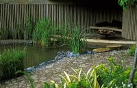 Walking Barefoot With Bradstone garden at Chelsea Flower Show 2006 - Recycled paving leading to under cover seating area with modern fire brazier beside pond