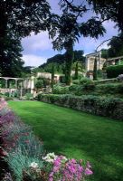 Italiante terraced formal garden with retaining walls, steps, tall Cupressus, columns and containers - Iford Manor