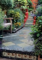 Mexican style courtyard garden with red and orange walls with stone paving and tile detailed path - Brighton