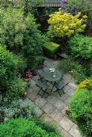 Overview of small back garden with paved area, table, chairs and containers 

