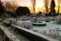 Formal garden in the frost in early morning light with low Buxus hedging beside path, edging borders - Shore Hall, Essex  