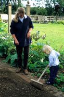 Woman and child sweeping path in vegetable garden - Pannells Ash Farm, Essex
