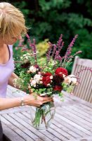 Woman arranging frshly picked flowers in vase on garden table