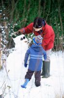 Mother and child making snowman in snow-covered garden