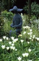 The Sitting Nun by Pete Lethbridge in the white garden at Glen Chantry with Tulipa 'Snow Star'