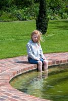 Girl with feet in the water of a Natural Swimming Pond on the edge of the Wimpole Hall Estate, Cambridgeshire