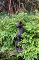 Bronze sculpture of Devon Rex cat at edge of pond