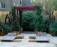 Roof garden with barleycorn gravel, bamboo chairs, red pergola and rusted steel sculpture
