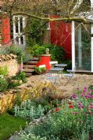 Patio with metal table and chairs, painted red walls and angled drystone walls, Wingwell nursery, Rutland