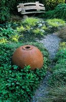Recovered metal fisherman's ball in ball garden Jura House Walled Garden with Gunnera magellanica, Carex elata 'Aurea', Viola odorata as ground cover - View to bench made from falled beech tree