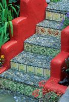 Red painted low walls of steps with pebble treads and tiled risers. Mediterranean Moorish style tiles and decorative pebbles - Brighton