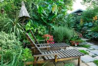 Exotic style garden with seating and tropical borders plants inc bamboo, ginger lily, Cordylines, Musa and shed in background