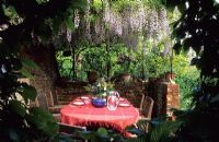 Seating and dining area in garden under Wisteria sinensis 'Rosea'