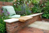 Built-in wooden seat in brick wall and a two-level water feature, raised beds with blue and white perennial planting in the Realistic Retreat garden, Chelsea 2007