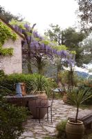 Outside eating area in Mediterranean garden with metal pergola with wisteria looking towards provencal hills