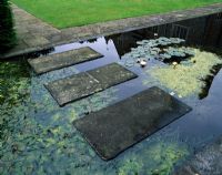 Stone slabs form a stepping stone bridge over a formal water garden planted with waterlilies