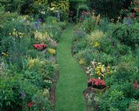 Herbaceous borders and grass walk with urns planted with Pelargonium 'Red Gables'