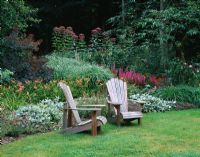 Two adirondack chairs in front of a border with Liatris, Hemerocallis and Eupatorium