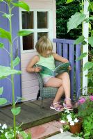 Young girl sitting reading on porch of painted wendy house 