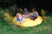 Children sitting on yellow circle deck surrounded by Bidens aurea, Stipa tenuissima and Carex buchananii