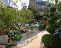 View onto small garden with italian hard limestone floor, blue table, white chairs and terracotta pots with box balls