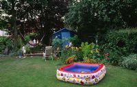Children playing in garden with blue summerhouse, hammock and paddling pool
