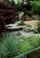 Stone bridge across gravel river with Acer in Japanese garden 