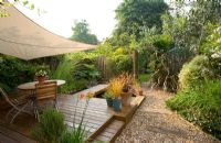 Exotic shade planting of grasses, Phormium, bamboo, rosemary and other foliage plants with canopy over decked dining area in small town gravel garden - London 