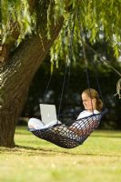 Teenage girl sitting in hanging chair with laptop