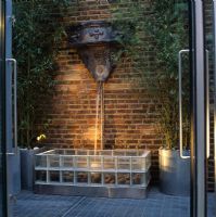 Water feature - water spout cascades onto sea-worn pebbles in fountain base of  transparent glass bricks in designer Stephen Woodhams' own garden