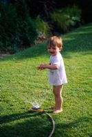 Toddler playing with a hosepipe in the garden.