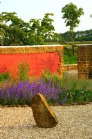 View across gravel garden to rock and red wall, border with Nepeta 'Walkers Low'
