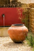 Gravel courtyard with large terracotta container, red wall, water spouts and trough