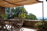 Stone terrace in old Tuscan farmhouse with wooden table and chairs and sun canopy - View to Tuscan landscape in Italy