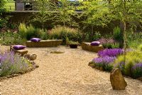 Gravel garden with seats made of rock, purple cushions and Salvia 'Wesuwe'
