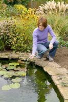 Woman spraying water from hosepipe onto surface of pond water, to top up pond and increase oxygen in water through bubbling